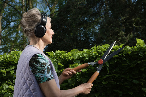 Woman wearing headphones and cutting hedge